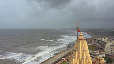 Rotierende-Luftaufnahme-Der-Safranfahne,-Die-Bei-Bewölktem-Wetter-Oben-Auf-Dem-Somnath-Mandir-Weht