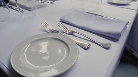 Fine-dining-restaurant-dinner-table-with-settings-on-white-table-cloth-steady-slow-motion-tilting-up-revealing-view