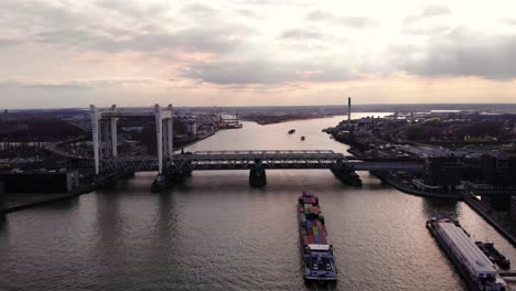 Aerial-Sunset-View-Of-Spoorbrug-Railway-Bridge-Over-Oude-Maas-With-Salute-Cargo-Container-Ship-Approaching