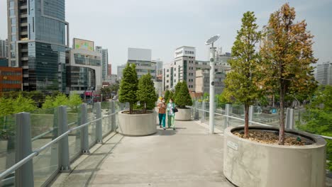 Two-frieds-wearing-face-masks-walk-along-the-Seoullo-7017-elevated-skygarden-in-Seoul,-South-Korea