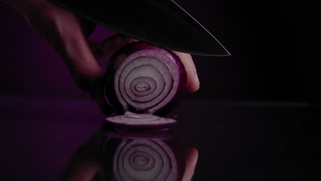 Close-up-cutting-a-fresh-red-onion-with-a-black-background-and-a-black-knife,-slow-motion