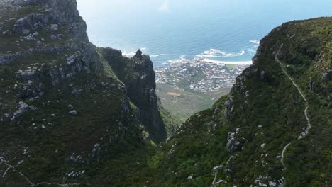 Aerial-Drone-Sot-of-Beautiful-Green-Mountain-Valley-looking-Down-onto-a-Sunny-Camps-Bay-Beach-in-Cape-Town