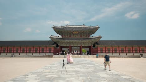 Una-Pareja-Coreana-Con-Ropa-Hanbok-Y-Máscaras-Protectoras-Toma-Una-Foto-Junto-Con-La-Puerta-Heungnyemun-Viajando-En-El-Palacio-Gyeongbokgung