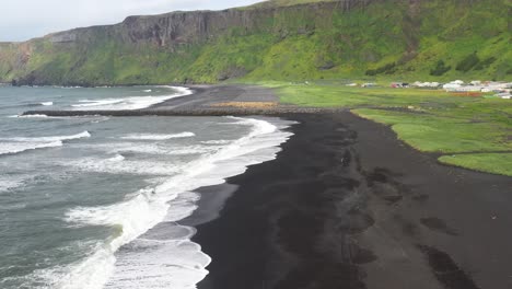 Black-sand-beach-with-waves-in-Vik,-Iceland-with-drone-video-moving-down