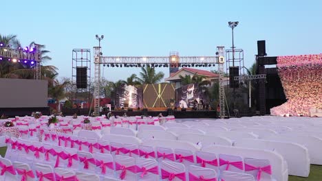 Decoración-De-Asientos-En-El-Escenario-De-La-Boda-Drone-Aéreo-Sobrevuela-El-Lugar-Rosa-Del-Jardín,-Sistema-De-Sonido-Y-Pantalla-Led