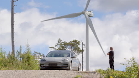 Un-Tesla-Model-3-Y-Su-Dueño-Frente-A-Un-Aerogenerador