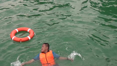 Man-wearing-a-life-jacket-in-a-swimming-pool,-swims-to-a-life-jacket-and-puts-it-on