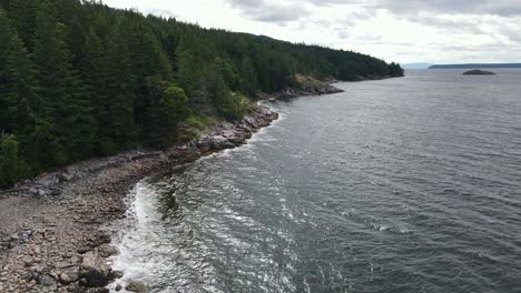 Aerial-view-of-pebbly-beach-and-rocky-coastline-with-conifer-trees-at-Dinner-Rock-Recreation-Site-in-British-Columbia