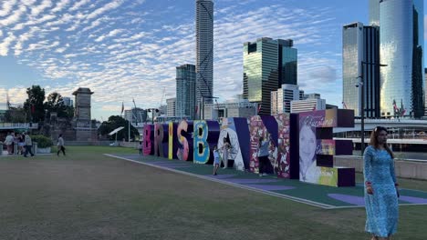 Niños-Y-Adultos-Felices-Divirtiéndose-Escalando-La-Icónica-Letra-De-Molde-De-La-Ciudad-De-Brisbane-Y-Tomando-Fotos-Memorables-Del-Hito-Con-El-Paisaje-Urbano-Del-Centro-Como-Telón-De-Fondo,-Queensland,-Australia