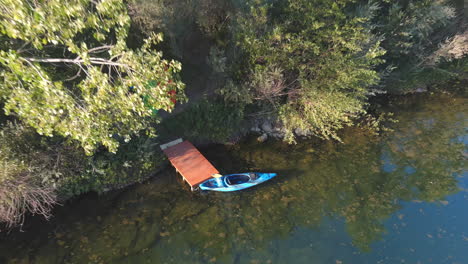 A-kayak-on-a-small-wooden-dock-on-the-Russian-River-in-Central-California---pull-back-ascending-aerial-view