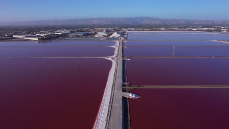 Flying-straight-over-pathway-in-maroon-colored-salt-ponds-in-East-bay-area,-Northern-California