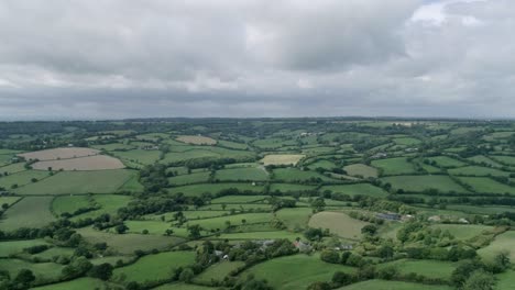 Aerial-fly-over-displaying-acres-of-farm-land-lined-with-woods-and-a-dramatic-cloud-filled-sky-at-Dumpdon-in-Devon,-England