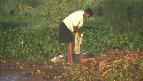 Mujer-Africana-Parada-En-Las-Orillas-Del-Lago-Victoria-Al-Sol-De-La-Mañana-Lavando-Ropa-Con-Agua-Del-Lago