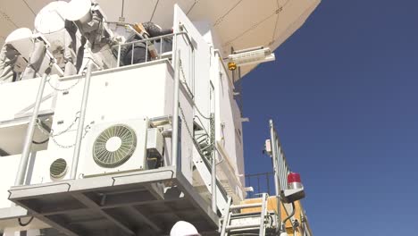 A-scientist-carrying-pipes-up-a-telescope,-another-scientist-following-with-other-gear