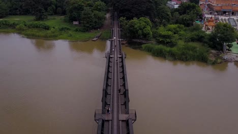 Toma-Aérea-De-Drones-Cruzando-El-Puente-Sobre-El-Río-Kwai,-Ferrocarril-De-La-Muerte-De-Tailandia,-Kanchanaburi,-Tailandia