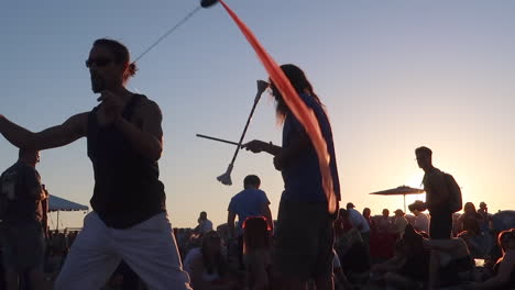 Primer-Plano-De-Un-Hombre-Actuando-Con-Cintas-Poi-En-Un-Festival-De-Música-Con-La-Puesta-De-Sol-En-El-Fondo-En-Cámara-Lenta