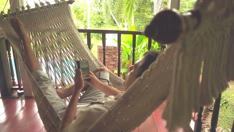 Adult-man-swinging-in-hammock-on-the-balcony-and-using-a-smartphone
