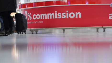 Passengers-with-rolling-suitcases-at-a-currency-exchange-kiosk-at-an-international-airport