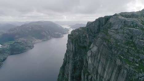 Aerial-Slomo-shot-of-Norwegian-Mountains,-revealing-Fjord-and-a-large-bridge-in-the-background,-during-Cloudy-weather