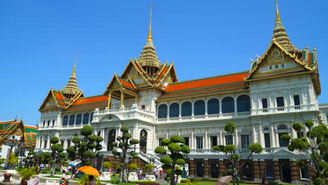 Bangkok-Thailand---Circa-Time-lapse-pan-shot-of-Grand-Palace-in-Bangkok,-Thailand-with-crowds-of-people-visiting-on-a-sunny-blue-sky-day,-view-of-architecture-and-Bonsai-trees