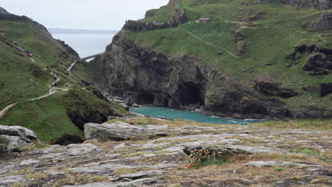 Touristen,-Die-Oben-Auf-Den-Klippen-Bei-Den-Ruinen-Von-Tintagel-Castle-Im-Norden-Von-Cornwall-Spazieren,-Mit-Tintagel-Beach-Und-Bay-Unten