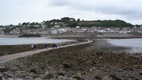 Turistas-Caminando-Por-La-Calzada-Que-Conduce-A-Marazion-Desde-El-Castillo-Medieval-Inglés-Y-La-Iglesia-Del-Monte-De-San-Miguel-En-Cornualles-En-Un-Día-Nublado-De-Primavera,-Imágenes-De-4k