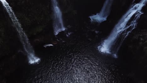 Rising-Drone-shot-above-a-beautiful-swimming-hole-with-four-gushing-waterfalls-pouring-into-it