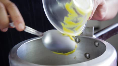 Female-hands-adding-mustard-from-a-small-transparent-bowl-with-a-spoon-inside-a-pressure-pan