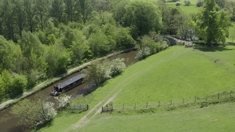 Eine-Luftaufnahme-Eines-Kanalboots,-Das-An-Einem-Sonnigen-Frühlingstag-Einen-Kanal-Hinunterfährt,-Der-Von-Der-Landschaft-Von-Yorkshire-Umgeben-Ist