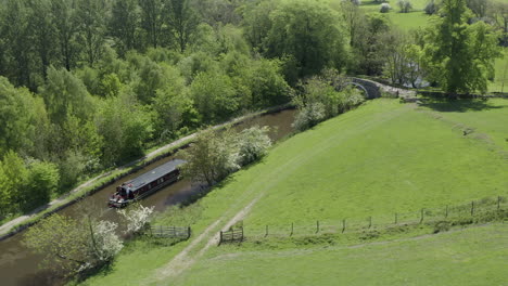 An-aerial-view-of-a-canal-boat-traveling-down-a-canal-surrounded-by-Yorkshire-countryside-on-a-sunny-spring-day