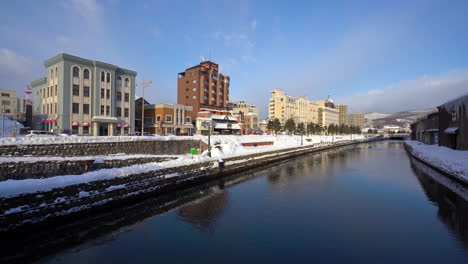 Hokkaido-Japan---Circa-side-pan-panoramic-shot-of-famous-Otaru-Canal-Hokaio-landmark-in-snow-winter,-sunny-blue-sky-daylight,-from-top-of-bridge