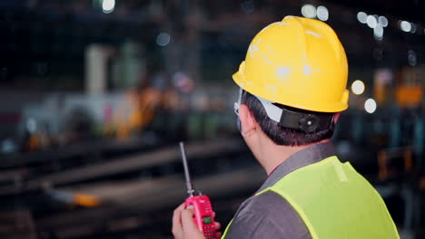 An-Engineer-at-steel-factory,-watching-the-work-and-talking-on-walkies-talkie,-Back-view-of-an-engineer,-wearing-safety-helmet-and-jacket