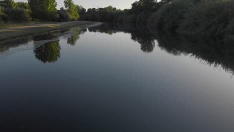 Drohnenaufnahme-Eines-Ruhigen-Flusses,-Umgeben-Von-Bäumen-Bei-Sonnenuntergang