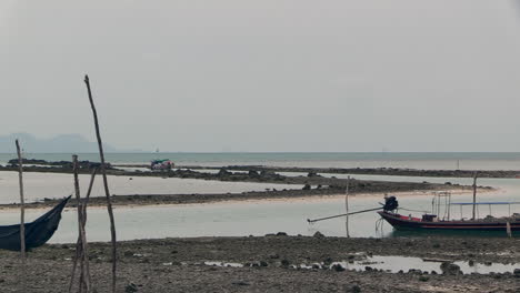 small-Thai-tourist-boat-enters-a-small-rocky-fairway-at-low-tide,-on-a-cloudy-day