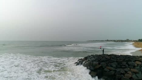 Group-of-Patriotic-youthful-men-hold-Indian-national-flag-standing-on-a-rocky-beach-front-with-waves-crashing