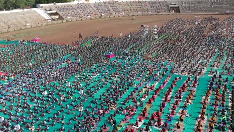 Aerial-footage-of-people-performing-Yoga-in-a-stadium-at-Ahmednagar,-India-on-the-occasion-of-International-Yoga-Day-along-with-school-students