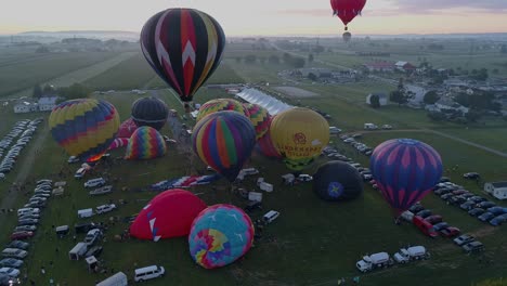 Vista-Aérea-De-Globos-Aerostáticos-Llenándose-Y-Despegando-En-Un-Festival-De-Globos-Aerostáticos-En-Una-Mañana-De-Verano