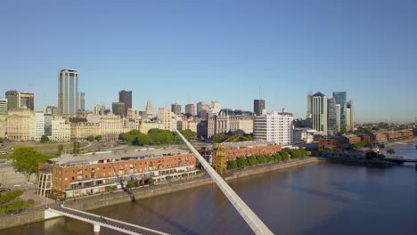 Lowering-shot-of-people-walking-on-Woman’s-Bridge-with-Puerto-Madero-buildings-in-background