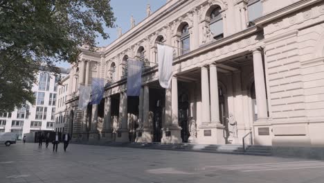 Static-shot-of-Stock-Exchange-in-Frankfurt-on-a-sunny-day-with-two-business-people-wearing-suit-in-walking-by,-Hessen,-Germany