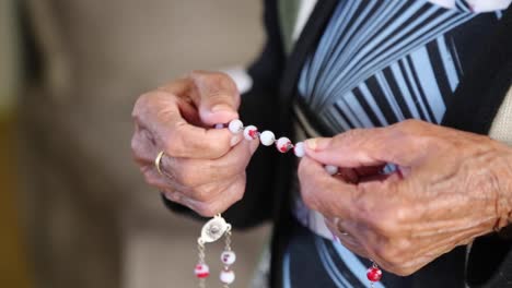 Eine-Frau-Hält-Ihren-Rosenkranz,-Während-Sie-Vor-Einem-Fernseher-Betet-Und-Dem-Priester-Zuhört