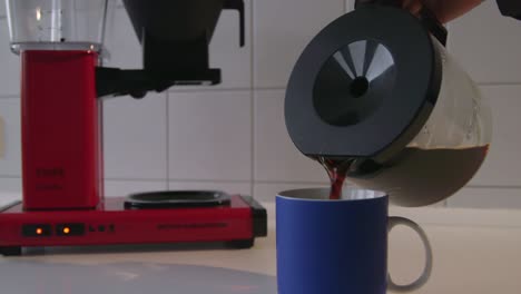 Caucasian-male-pouring-coffee-from-a-vintage-coffee-maker-into-a-blue-cup