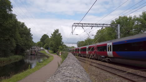 Toma-Estática-De-Un-Tren-Del-Norte-Que-Pasa-Por-Las-Esclusas-Del-Canal---Peatones-Mientras-Viaja-Hacia-Leeds-En-Un-Día-De-Verano-En-Cámara-Lenta