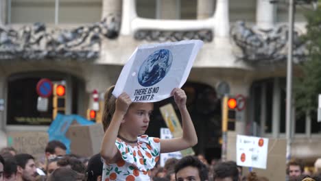 Una-Niña-Sostiene-Un-Cartel-De-Protesta-Contra-El-Cambio-Climático-Sobre-La-Multitud-Cabalgando-Sobre-Los-Hombros