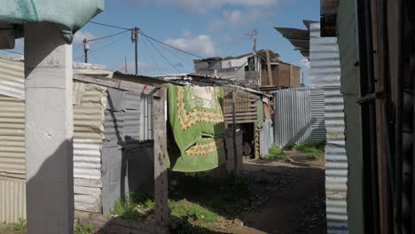 Backstreets-between-shacks-in-township-with-blanket-flapping-in-wind,-South-Africa