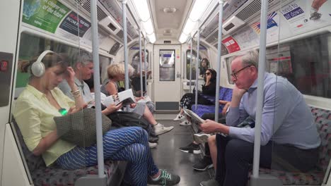 Hombre-Mayor-Entrando-Al-Tren-Subterráneo-De-Londres,-Sentado-Y-Leyendo-El-Periódico