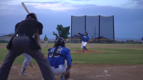 Clip-En-Cámara-Lenta-Durante-Un-Partido-De-Béisbol-De-Ligas-Menores-Desde-Detrás-Del-Plato-De-Home-Durante-El-Lanzamiento-Y-El-Golpe,-Panorámica-Sobre-El-Corredor-En-El-Camino-A-La-Primera-Base