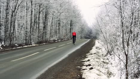 Stabile-Aufnahme-Hinter-Der-Perspektive-Eines-Ciclyst,-Der-Auf-Einer-Leeren-Straße-Durch-Einen-Verschneiten-Wald-Geht