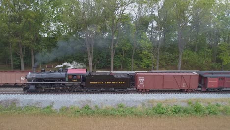 Vista-Aérea-De-Un-Tren-De-Pasajeros-De-Locomotora-De-Vapor-Tirando-Lentamente-De-Un-Revestimiento-Pasando-Un-Tren-De-Carga-De-Vapor-Con-Humo-Y-Vapor