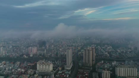 Early-morning-urban-drone-flight-orbit-around-high-rise-buildings-and-major-roads-and-bridge-with-heavy-fog-and-low-clouds-in-clockwise-direction