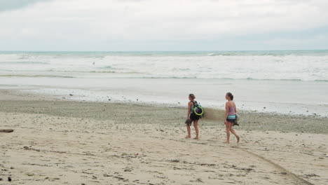 Slow-Motion-Back-Shot-Two-Young-Female-Surfers-Holding-Surf-Board-Walk-Along-the-Beach-in-Tambor,-Costa-Rica